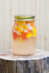 Fresh lemonade from lemon and grapefruit and orange in a jar on a wooden stump.