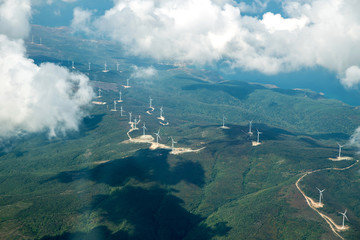 Fototapeta premium Panorama skyline view of cloudy blue sky from airplane window over wind farm landscape background. Wind turbines renewable power energy stations. Environmentally friendly renewable energy windmill.
