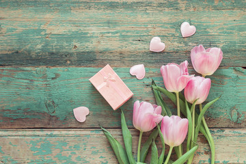 Pink tulips, hearts and gift box on a turquoise grunge wooden background.