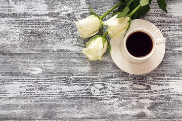 Coffee cup and white rose flowers on wooden table background. Top view, copy space.