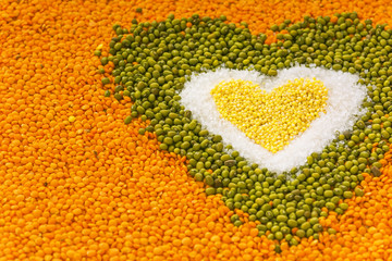 Heart shape background made of mixed wheat grains, white salt, green mung beans, orange red lentils. Dry cooking ingredients for a healthy diet soup.