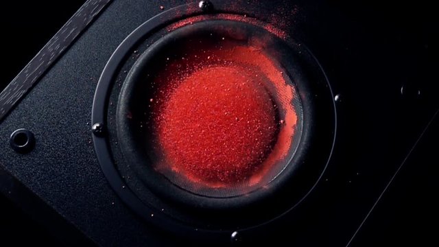 Shaking subwoofer throws orange dust in the air. Super slow motion video