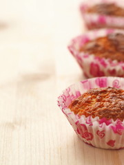 Three muffins in a row on the right hand side of wooden table. Homemade pastry. Vertical. Copy space for your text. Selective focus on the front.
