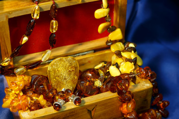A lot of jewelry from authentic Baltic amber with a big pendant in the center in wooden chest on a blue background satin.