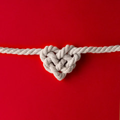 White rope in heart shape knot on red background. Love concept. Flat lay. - obrazy, fototapety, plakaty