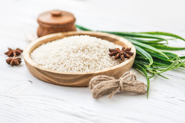rice in wooden plate and anise on white wooden background. Rice and spices in ecological container. Set for cooking. Set for spa.