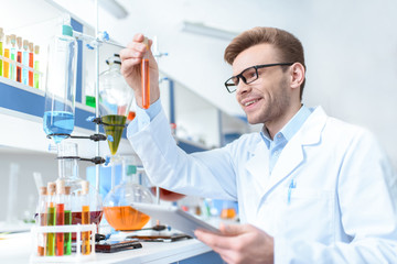 Young smiling man scientist holding digital tablet and looking at test tube in lab