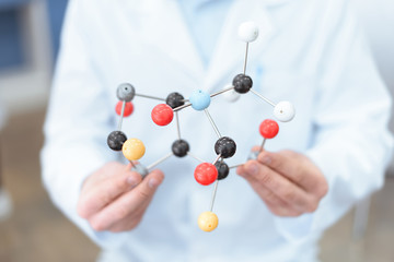 Close-up partial view of scientist in white coat holding molecular model