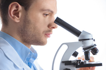 side view of concentrated man scientist looking through microscope on white
