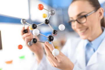 smiling scientist holding molecular model in laboratory, focus on foreground