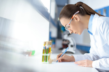 side view of scientist writing down test results while working in laboratory