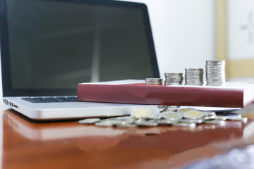 Business concept. Closeup stack of coins, laptop  and old book on wooden table.