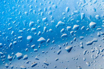 Several water drops on transparent glass and on blue background