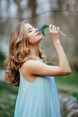 attractive model in blue dress smell snowdrop flowers in the spring forest