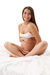 Fototapeta na wymiar Pregnant woman posing in studio sitting on bed