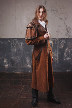Handsome male in brown cloak, Steam punk style. Retro man portrait over grunge background.