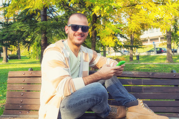 Obraz premium Man using cellphone on a bench in the park.