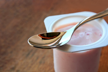 Strawberry pink yogurt in white plastic cup on a wooden rustic background with spoon on it with copy space.