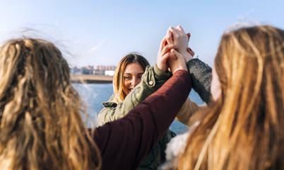 Four happy friends raising their hands together