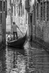 Fototapeta na wymiar Venetian gondolier navigates with his gondola in a narrow canal in the historic center of Venice, Italy. in black and white