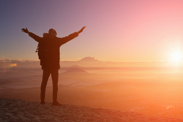 Fototapeta premium male traveler is standing on top of a mountain with a backpack and put his hands up