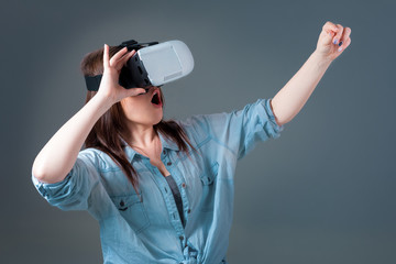 Emotional young woman using a VR headset and experiencing virtual reality on grey background