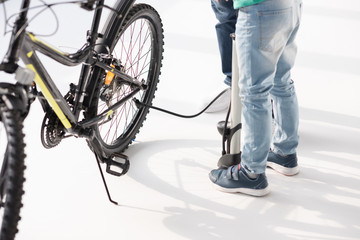 Low section of father and son inflating bicycle tire with pump on white