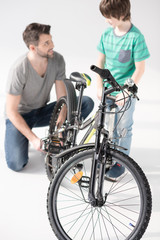 Fototapeta na wymiar Happy father and son inflating bicycle tire looking at each other