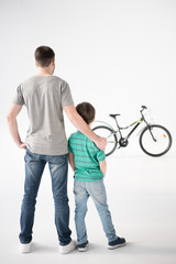 back view of father and son looking at bicycle on white