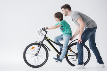 Obraz premium side view of father helping son to ride bicycle on white