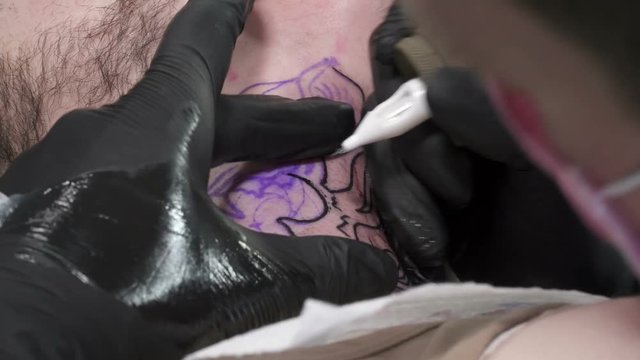 A young man with beard is having tatoo made on his neck