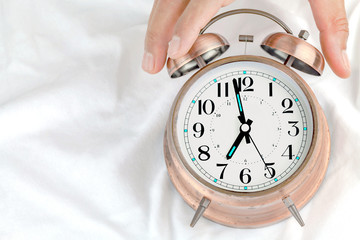 Alarm clock  on a bed with hands of a man holding a clock.