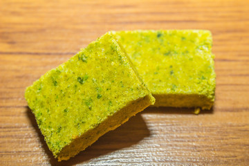 Dehydrated bouillon stock cube salty meat and vegetables aromatic yellow spice, ingredient single whole condiment portion wrapped, open in paper pack on wooden background