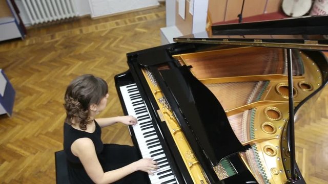 Overhead shot of a happy young woman playing grand piano. Pianist musician plays piano at a concert, fingers touching piano keys. Fingers typing on piano keys. Top view