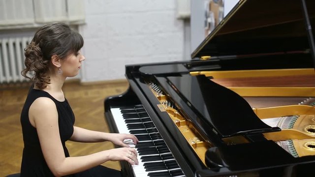 Happy talented young lady playing grand piano. Pianist musician plays piano at a concert, fingers touching piano keyboard. Fingers typing on piano keys