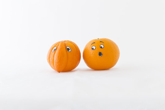 Fresh oranges with funny faces in front of white background. One orange has a huge nose