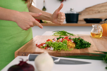 Close up of  woman's hands cooking in the kitchen. Housewife offering ​​fresh salad with thumbs up. Vegetarian and healthily cooking concept