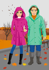 young couple wearing raincoats standing in park in autumn