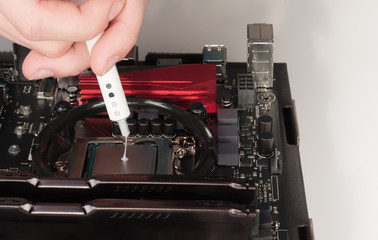 Close up of man hands with syringe applying thermal paste on the CPU processor on motherboard.