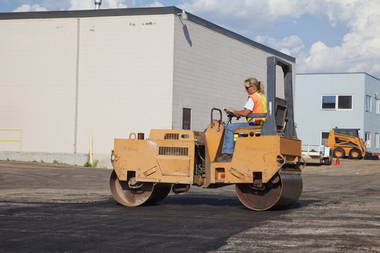 Female operator driving steam roller repairing pot holes in a parking lot; Edmonton, Alberta, Canada