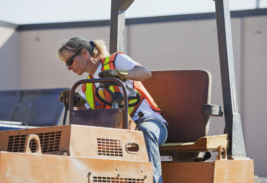 Woman driving stream roller repairing pot holes in parking lot; Edmonton, Alberta, Canada
