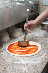 Male chef smears red sauce spicy pizza. Raw dough preform. Production and delivery of pizza