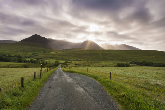 View along a road early in the morning with the rising sun behind the Black Cuillin Ridge; Glen Brittle, Skye, Scotland