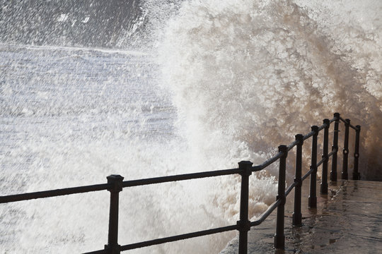 Waves splashing and crashing into railing and stairs in Jacob's Ladder Bay; Sidmouth, South Devon, England