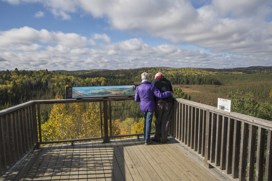 Mature couple overlooking Sunday Creek from the Algonquin Park visitor centre observation deck on a sunny afternoon in autumn; Ontario, Canada