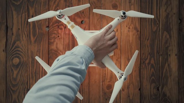 Top view, small white drone with 4k camera landed on wooden rustic table, blinking with navigation led lamps. Male hands turn it off after using
