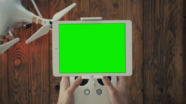 Top view, male hands gently use drone remote controller to control quadrocopter flight. Big white smart tablet with chromakey on screen mounted on special holder
