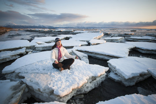 Woman practicing meditation on ice chunks stacked against the Homer Spit, Southcentral Alaska