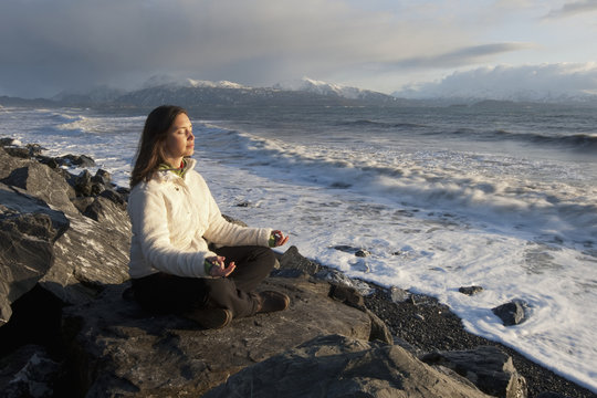 Woman practicing meditation on a rocky beach, Homer Spit, Southcentral Alaska