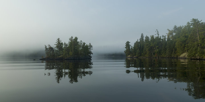 Fog over a tranquil Lake of the Woods and trees reflected along the shoreline; Ontario, Canada